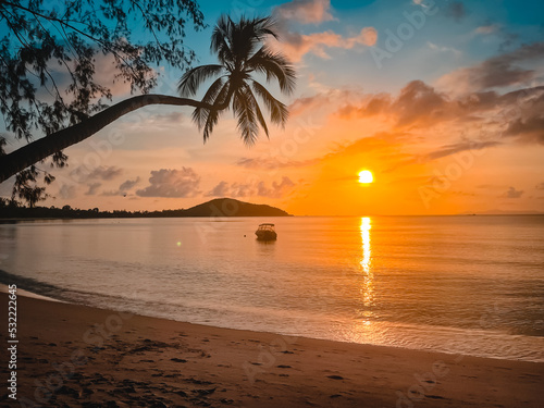 Bright sunset tropical beach, calm sea water, sand beach, fishing boat silhouette in orange sun light. Palm tree, sunrise colorful background. Amazing island landscape. Resort vacation, travel concept