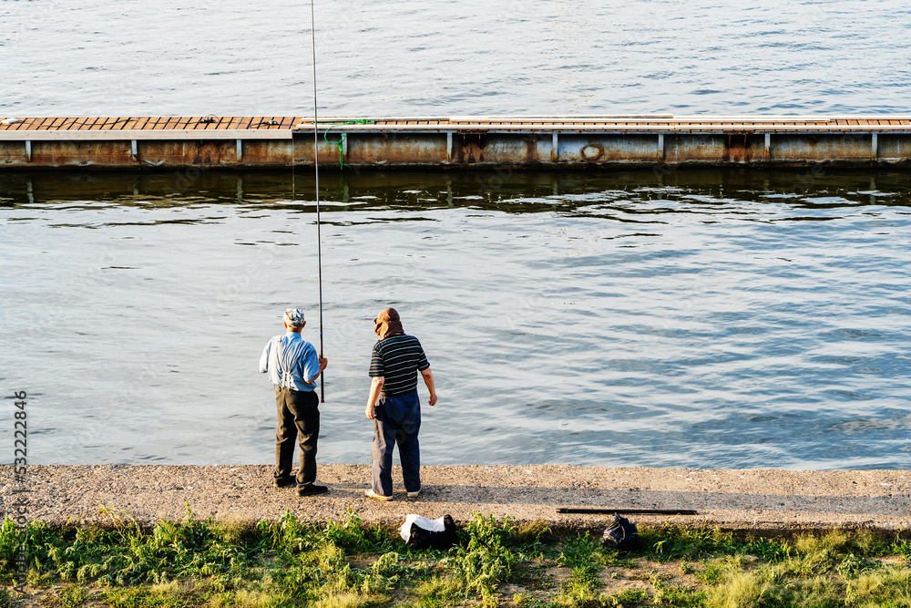 Two pensioners are fishing on the river bank. Summer fishing in the city near the mooring pantones.