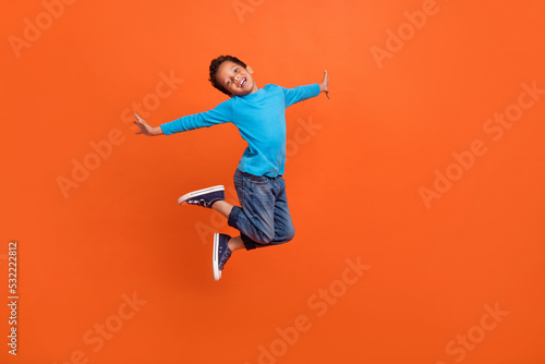 Full length photo of adorable little pupil boy jumping school shopping poster wear trendy blue clothes isolated on orange color background