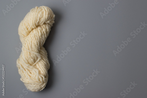 knitting and wool craft background - lovely cream and white natural coloured skein of art yarn pure wool on grey background with copy space 