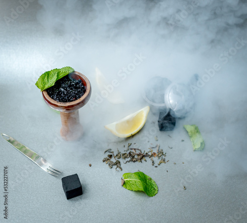 Hookah bowl with aromatic black tobacco with lemon and mint on gray table with smoking accessories. Hookah smoking in a hookah lounge. Tea and coconut charcoal