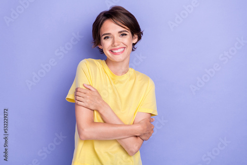 Photo of young gorgeous adorable girl wear bright yellow t-shirt toothy smile hug herself lovely isolated on pastel purple color background