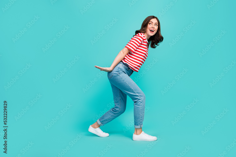 Full length photo of crazy pretty lady arm hold big size ad carry look empty space striped stylish wear isolated on cyan color background Full length photo of crazy pretty lady arm hold big size ad carry look empty space striped stylish wear isolated on cyan color background
