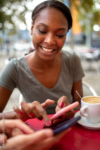 Black woman using mobile phone while sitting with her friend at coffee shop