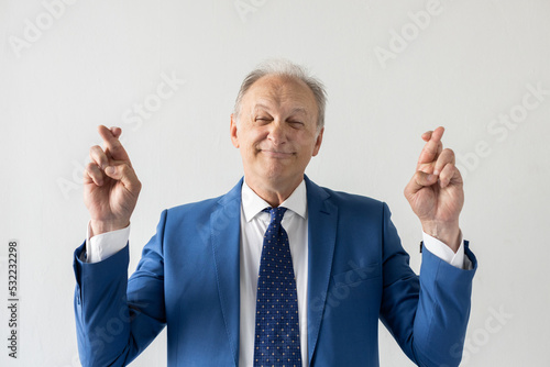 Portrait of dishonest mature businessman crossing fingers. Deceitful senior manager wearing formalwear looking at camera and smiling against white background. Liar concept photo