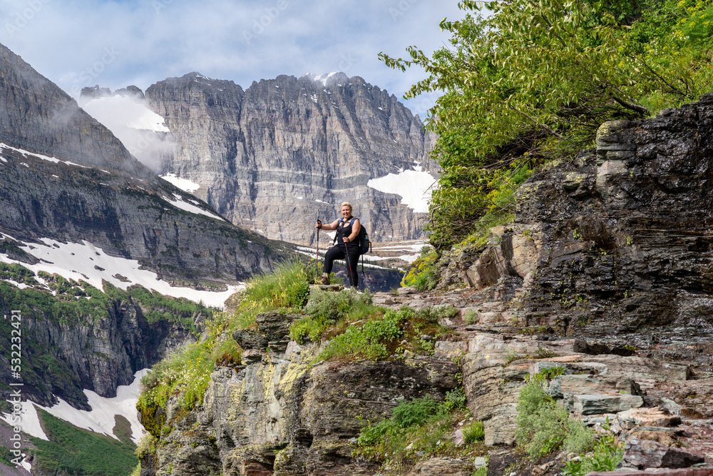 Happy blonde woman hiker stands on a cliff enjoying the view along the Grinnell Glacier Trail in Glacier National Park