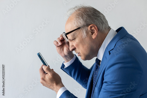 Bilde på lerret Mature businessman taking off glasses and reading message on mobile phone