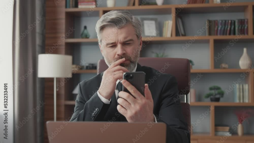 Middle-aged bearded businessman uses smartphone while sitting in office. A stylish businessman looks at the news, studies trends. Middle-aged bearded businessman uses smartphone while sitting in office. A stylish businessman looks at the news, studies trends.