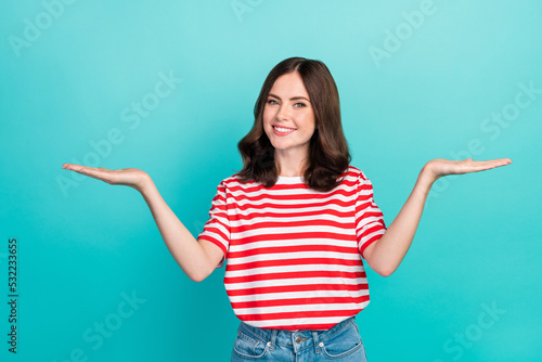Photo of young cute nice pretty gorgeous woman wear red striped t-shirt hold palms compare products difference smile isolated on cyan color background
