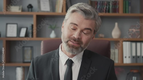 Middle-aged businessman talking directly into the camera via online video call on his laptop while sitting at his desk