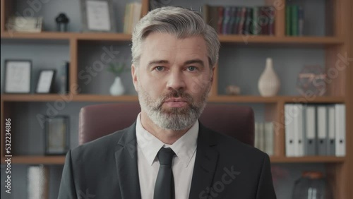 Successful middle-aged businessman talking via online video call on his laptop while sitting at a desk and working in his office. Confident man talking to the camera