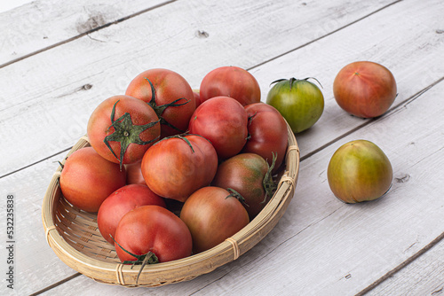 fresh red tomato on wicker basket on gray background.