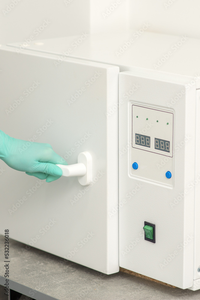 Beautician in protective gloves close the door of the machine for disinfection of tools before the medical procedures Beautician in protective gloves close the door of the machine for disinfection of tools before the medical procedures