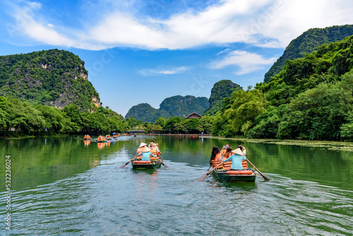 Fototapeta Tourists sitting on rowing boats enjoy the beautiful scenery of rivers and mountains in Trang An, Ninh Binh province, Vietnam
