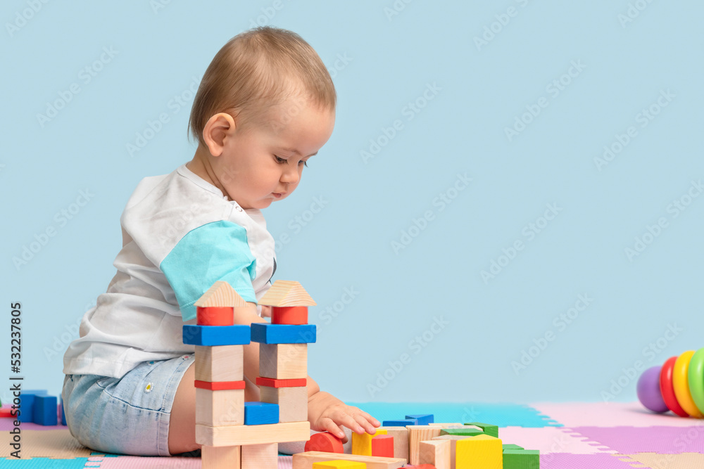 Toddler 12-17 months playing with a designer of colorful wooden cubes sitting on the floor in the playroom. Copy space Toddler 12-17 months playing with a designer of colorful wooden cubes sitting on the floor in the playroom. Copy space