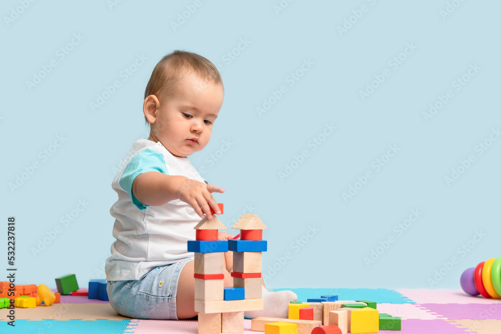 Toddler 12-17 months old builds a tower of wooden cubes sitting on the floor in the playroom Toddler 12-17 months old builds a tower of wooden cubes sitting on the floor in the playroom