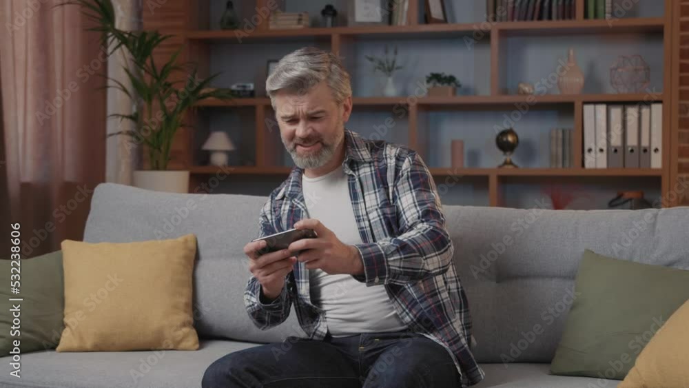 Middle-aged man playing mobile games at home on the sofa, enjoying the game process, disappointed by losing and looking forward to revenge Middle-aged man playing mobile games at home on the sofa, enjoying the game process, disappointed by losing and looking forward to revenge