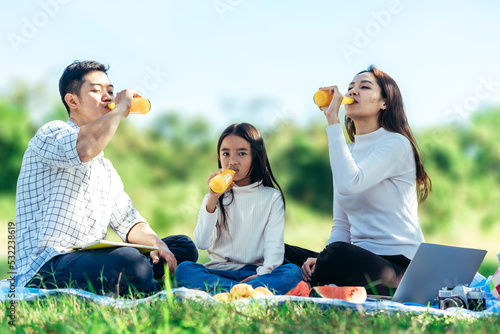 Happy asian family in the garden, Father, Mother and doughter. They are having fun drinking orange juice in holiday.