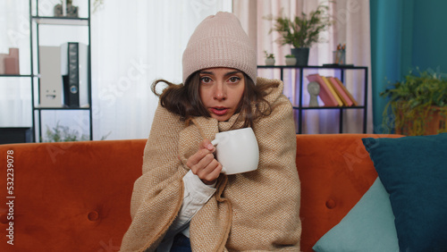 Cuadro en lienzo Sick girl wear hat wrapped in plaid sit alone shivering from cold on sofa drinking hot tea in unheated apartment without heating due debt