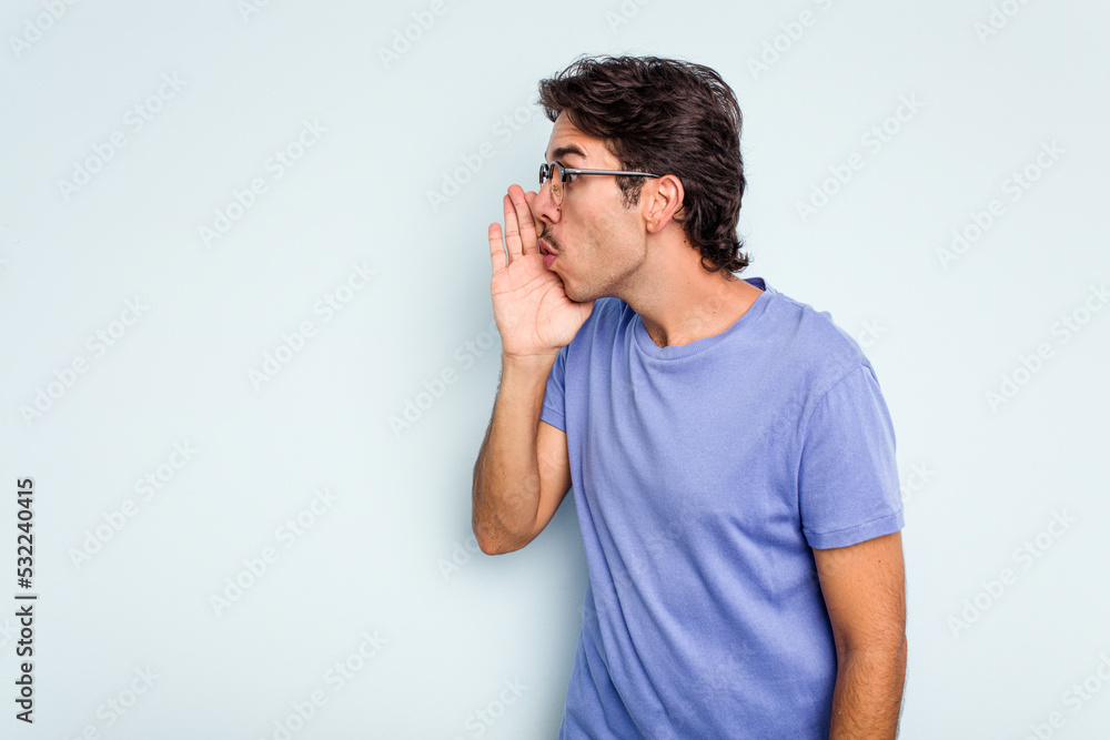 Young hispanic man isolated on blue background is saying a secret hot braking news and looking aside Young hispanic man isolated on blue background is saying a secret hot braking news and looking aside