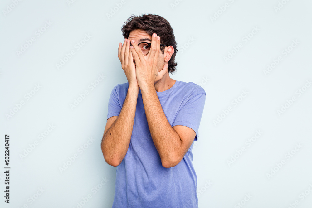 Young hispanic man isolated on blue background blink through fingers frightened and nervous. Young hispanic man isolated on blue background blink through fingers frightened and nervous.