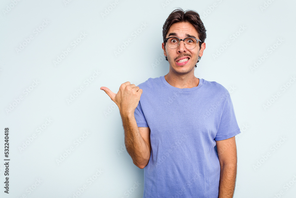 Young hispanic man isolated on blue background shocked pointing with index fingers to a copy space. Young hispanic man isolated on blue background shocked pointing with index fingers to a copy space.