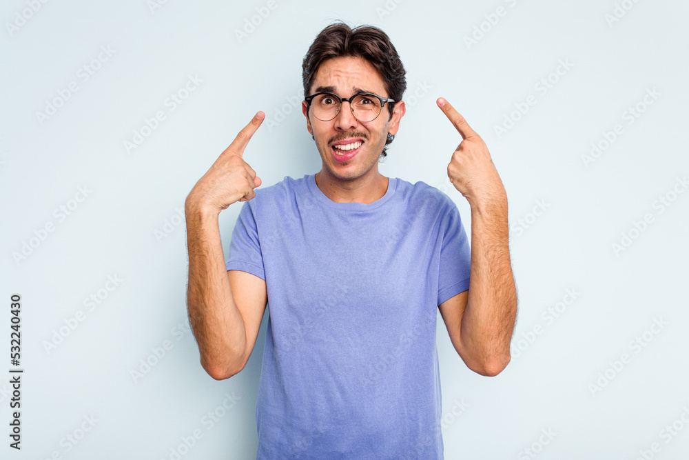 Young hispanic man isolated on blue background showing a disappointment gesture with forefinger. Young hispanic man isolated on blue background showing a disappointment gesture with forefinger.