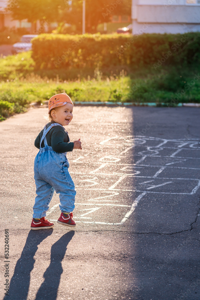 Fototapeta premium A kid plays hopscotch on the playground during sunset