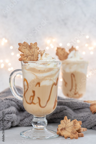 Pumpkin spice latte in a glass mug with caramel and cinnamon cookies with Autumn decoration