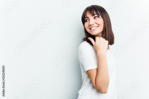 Young caucasian woman isolated on white background points with thumb finger away, laughing and carefree.