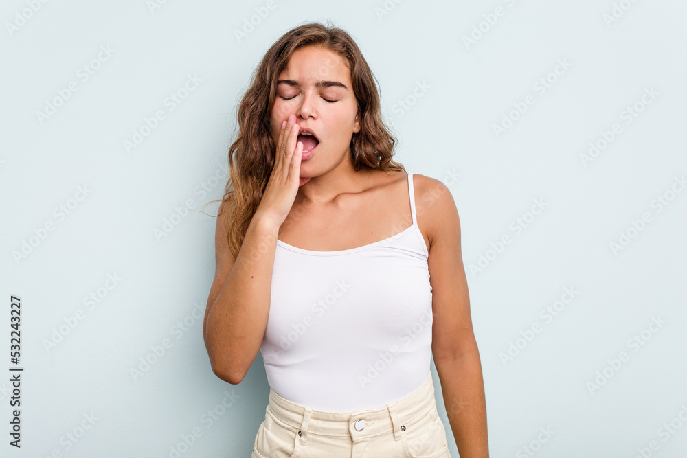 Young caucasian woman isolated on blue background yawning showing a tired gesture covering mouth with hand. Young caucasian woman isolated on blue background yawning showing a tired gesture covering mouth with hand.