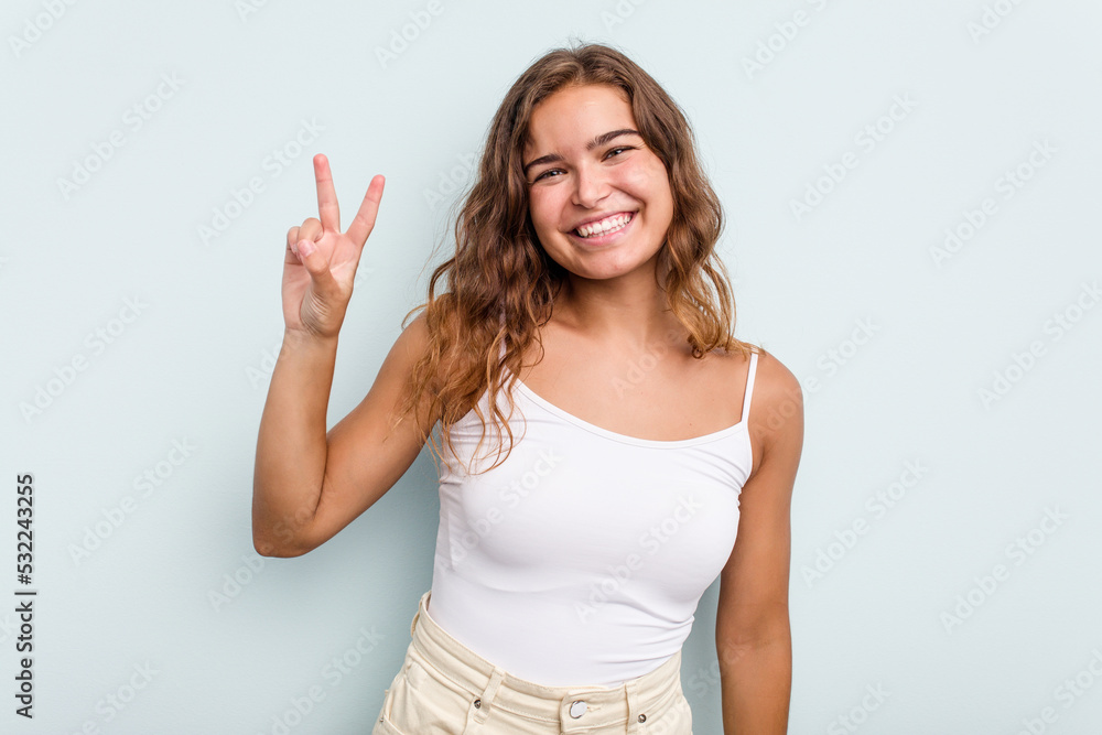 Young caucasian woman isolated on blue background joyful and carefree showing a peace symbol with fingers. Young caucasian woman isolated on blue background joyful and carefree showing a peace symbol with fingers.