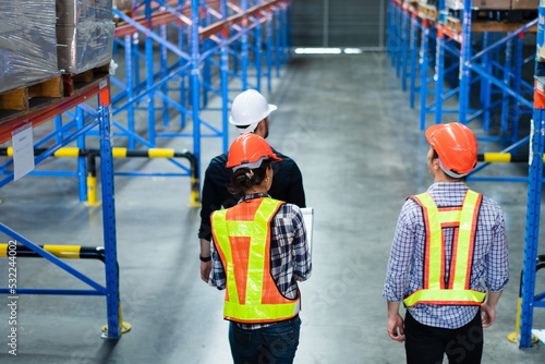 Group of warehouse workers walking and checking on stock before shipping delivery in the factory. Staff with client visiting at distribution center. Logistic business career.