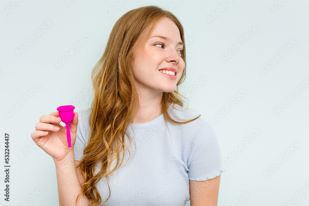 Young caucasian woman holding menstrual cup isolated on blue background looks aside smiling, cheerful and pleasant. Young caucasian woman holding menstrual cup isolated on blue background looks aside smiling, cheerful and pleasant.