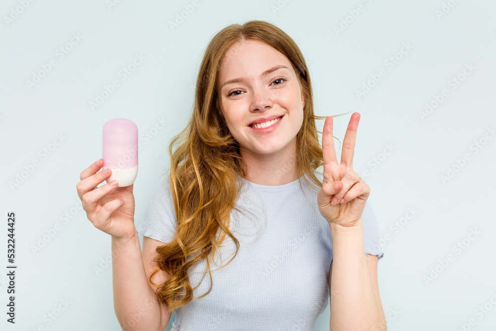 Young caucasian woman holding deodorant isolated on blue background showing number two with fingers. Young caucasian woman holding deodorant isolated on blue background showing number two with fingers.