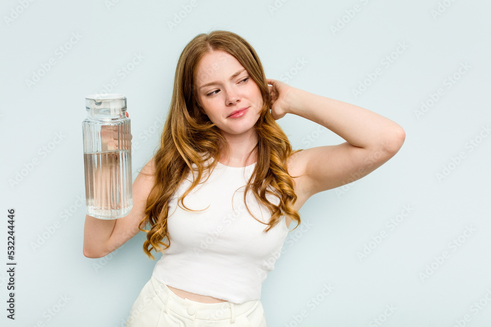 Young caucasian woman holding jar of water isolated on blue background touching back of head, thinking and making a choice. Young caucasian woman holding jar of water isolated on blue background touching back of head, thinking and making a choice.