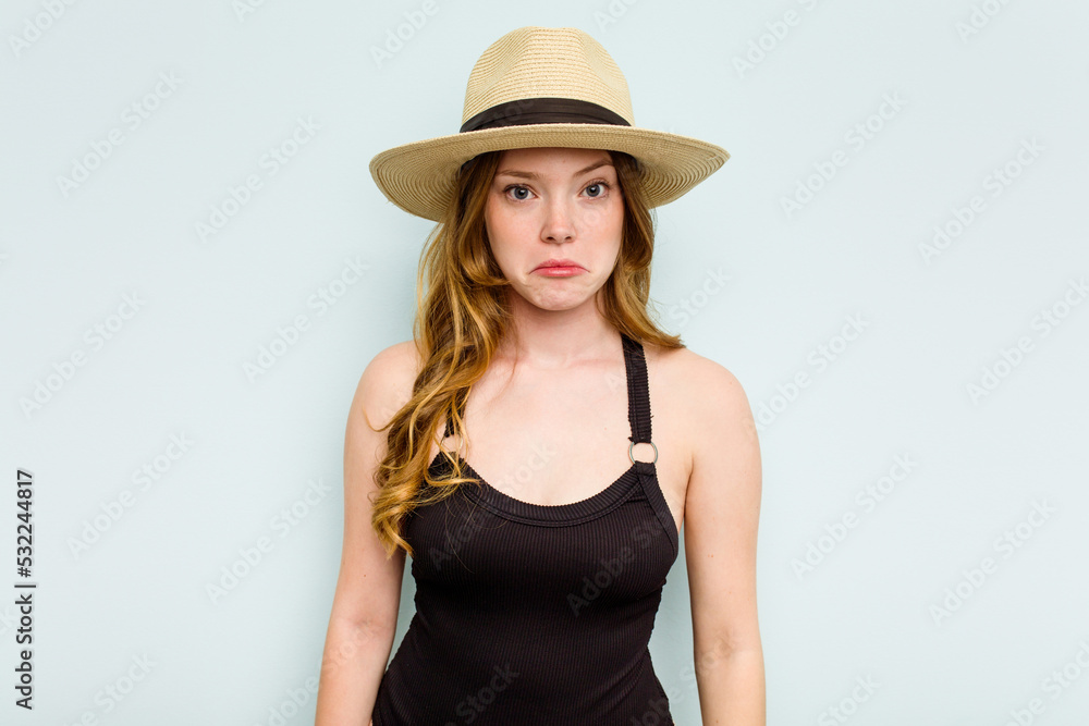 Young caucasian woman going to the beach isolated on blue background shrugs shoulders and open eyes confused. Young caucasian woman going to the beach isolated on blue background shrugs shoulders and open eyes confused.