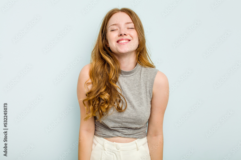 Young caucasian woman isolated on blue background laughs and closes eyes, feels relaxed and happy.