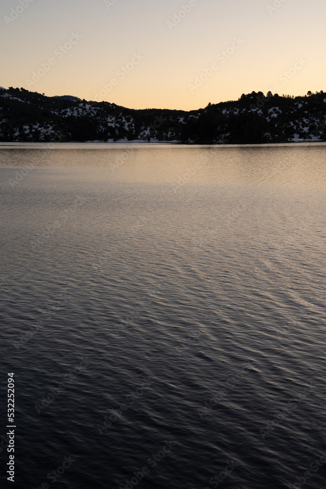 View of the lake and mountains at nightfall. Beautiful sunset colores in the water and sky. View of the lake and mountains at nightfall. Beautiful sunset colores in the water and sky.