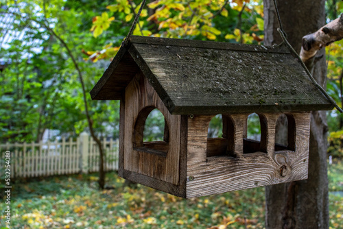 A bird feeder hangs in the garden. Blurred garden background on an autumn day. Table for birds. Bird feeders among the trees on a sunny day. Feeder for hungry birds. Autumn colors in the garden. © Vladimir