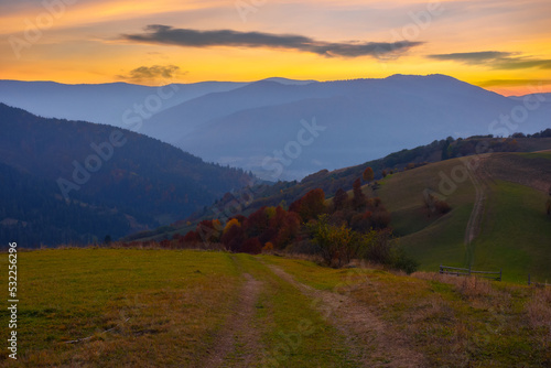 mountainous countryside at dusk. green grassy rolling hills on an autumn evening. carpathian rural scenery. view in to the distant ridge beneath a glowing sky with clouds