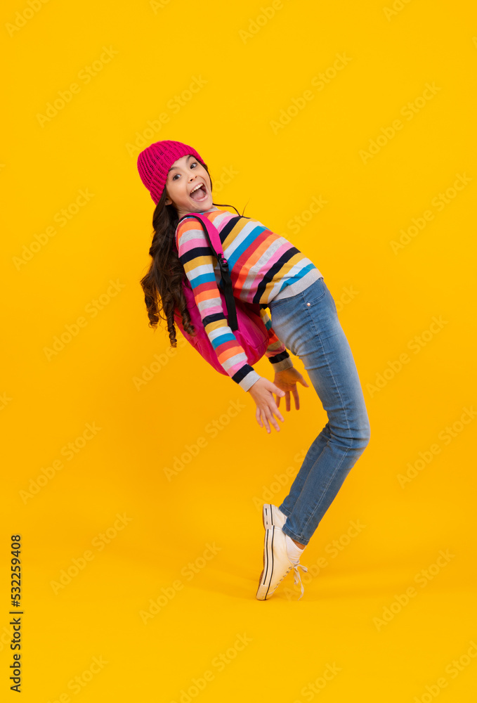 Funny school girl child student with backpack and warn hat, isolated yellow background. Learning and knowledge education concept. Autumn school. Happy teenager, positive and smiling.