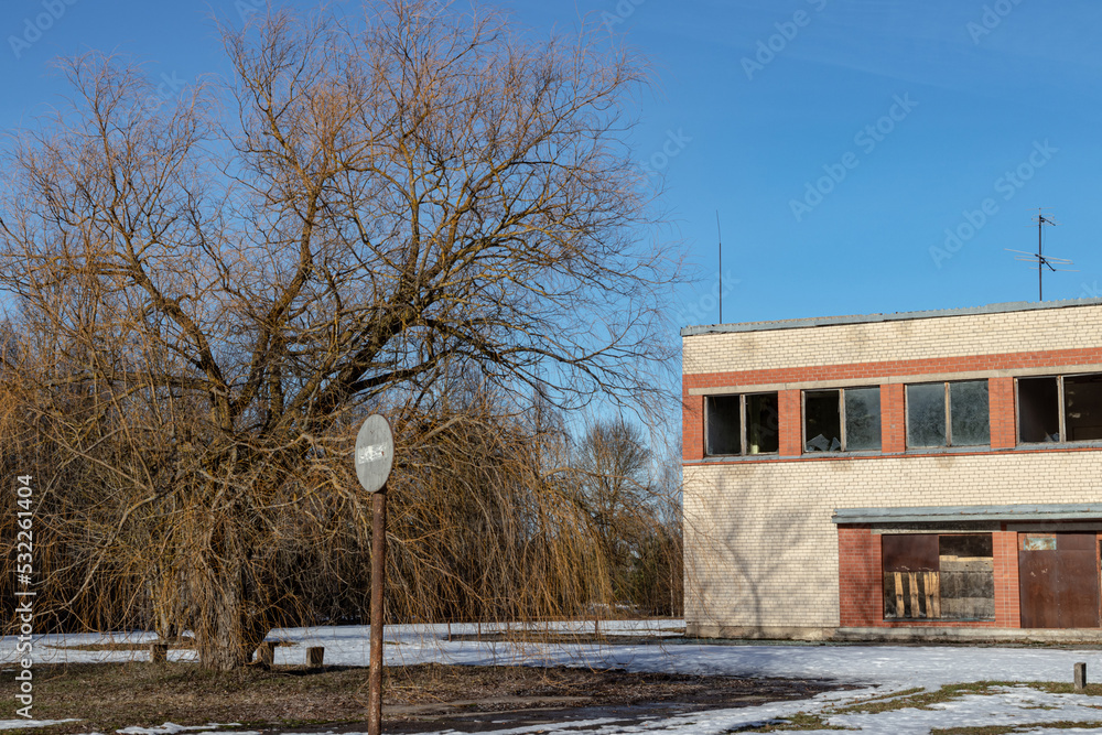 abandoned brick building in Latvia village in winter, leafless bare willow tree, snow covered asphalt, old dont enter sign abandoned brick building in Latvia village in winter, leafless bare willow tree, snow covered asphalt, old dont enter sign