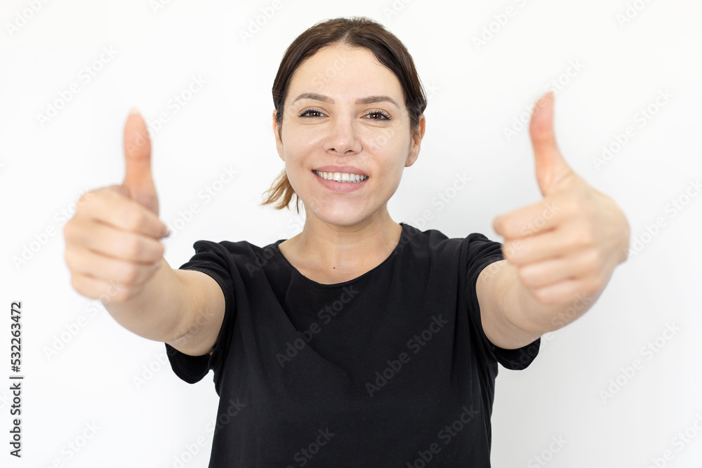 Smiling woman showing thumbs up gesture at camera. Happy Caucasian woman looking at camera while standing on white background. Emotion, expression, gesture, studio shot, agreement concept Smiling woman showing thumbs up gesture at camera. Happy Caucasian woman looking at camera while standing on white background. Emotion, expression, gesture, studio shot, agreement concept