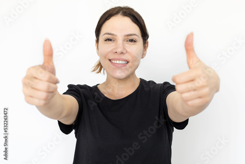 Smiling woman showing thumbs up gesture at camera. Happy Caucasian woman looking at camera while standing on white background. Emotion, expression, gesture, studio shot, agreement concept © KAMPUS