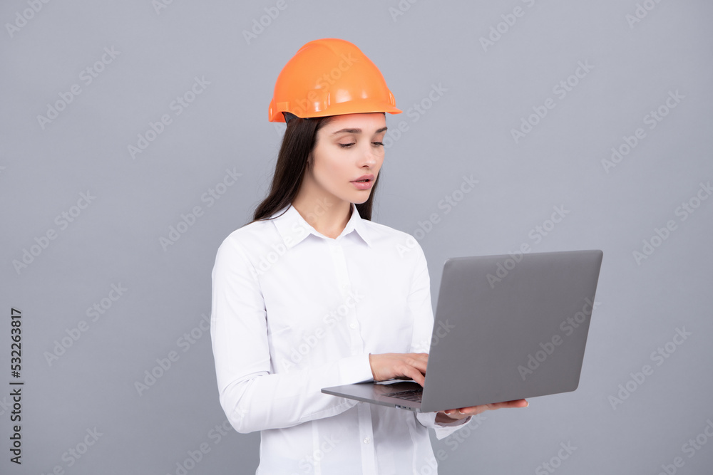 Young woman in helmet hold laptop computer on gray background. Architect businesswoman in helmet thinking, young caucasian female in work as constructor engineer. Young woman in helmet hold laptop computer on gray background. Architect businesswoman in helmet thinking, young caucasian female in work as constructor engineer.