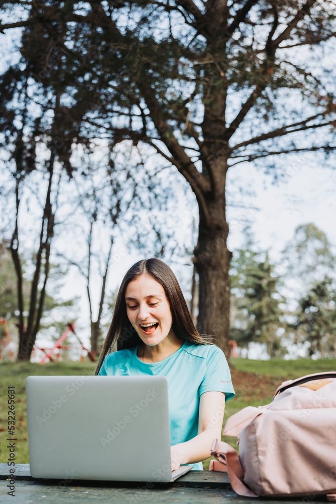 Female university student laughing and using her laptop in college campus park. Turquoise tshirt Female university student laughing and using her laptop in college campus park. Turquoise tshirt