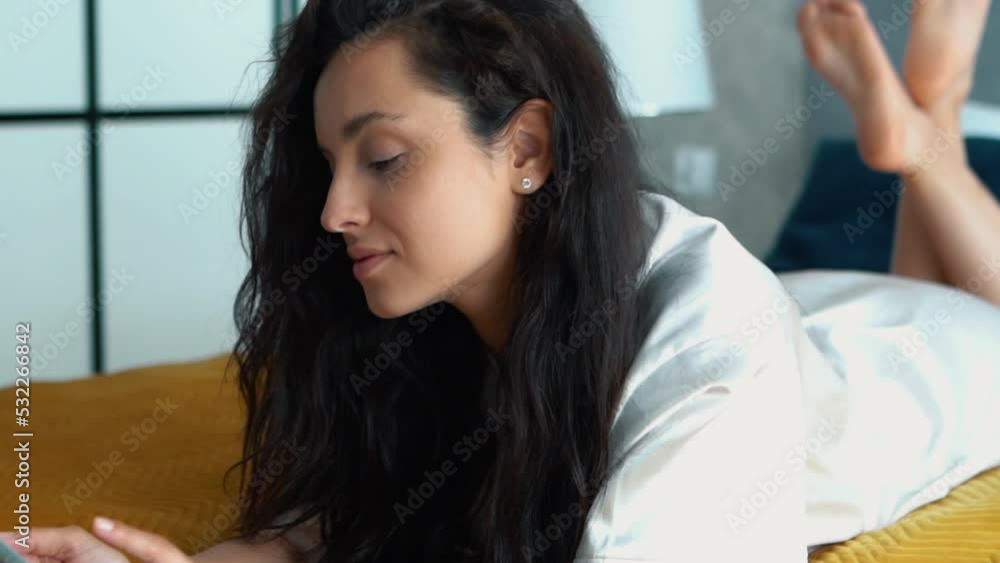 Caucasian young beautiful woman typing on smartphone browsing online in apartment. Close up of dark-haired happy female resting at home in bedroom using mobile phone. Slow motion Caucasian young beautiful woman typing on smartphone browsing online in apartment. Close up of dark-haired happy female resting at home in bedroom using mobile phone. Slow motion