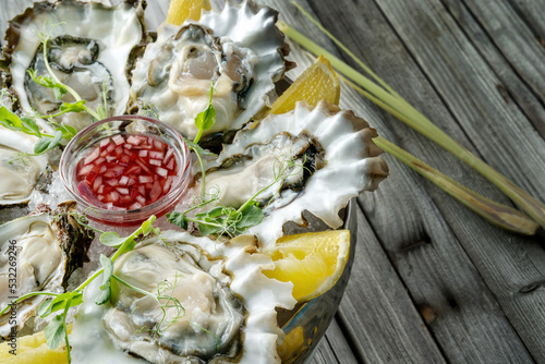 Large fresh oysters with sweet dipping sauce and lemons on a plate of crushed ice.