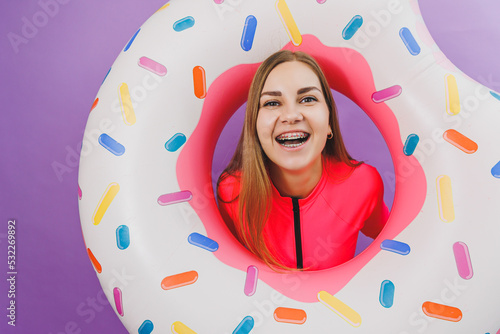 Attractive emotional woman in stylish pink swimsuit with donut inflatable ring on plain background. Beach fashion